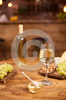 Glass and bottle of white wine next to fresh grapes on wooden table in a vintage pub