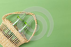 Glass bottle in wicker basket on green background. Sustainable lifestyle. Undertone. Copy space photo