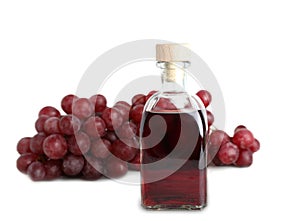 Glass bottle with wine vinegar and fresh grapes on white