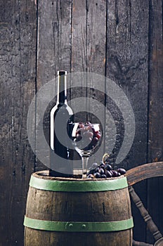 Glass and bottle of wine on a wooden barrel. Burnt, black wooden background. Vintage. Copyspace for a text. Grapes and green vine.