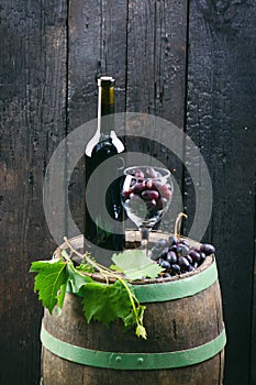 Glass and bottle of wine on a wooden barrel. Burnt, black wooden background. Vintage. Copyspace for a text. Grapes and green vine.