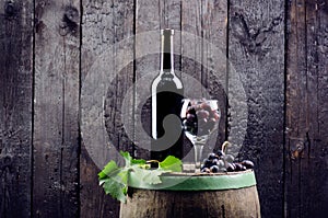 Glass and bottle of wine on a wooden barrel. Burnt, black wooden background. Vintage. Copyspace for a text. Grapes and green vine.