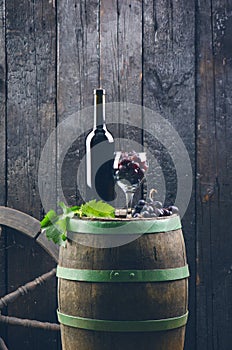 Glass and bottle of wine on a wooden barrel. Burnt, black wooden background. Vintage. Copyspace for a text. Grapes and green vine.