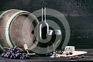 Glass and bottle of wine on a wooden barrel. Burnt, black wooden background. Vintage. Copyspace for a text. Grapes and green vine.