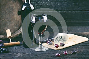Glass and bottle of wine on a wooden barrel. Burnt, black wooden background. Vintage. Copyspace for a text. Grapes and green vine.