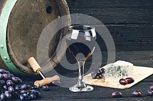 Glass and bottle of wine on a wooden barrel. Burnt, black wooden background. Vintage. Copyspace for a text. Grapes and green vine.