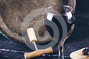 Glass and bottle of wine on a wooden barrel. Burnt, black wooden background. Vintage. Copyspace for a text. Grapes and green vine.