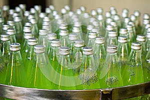 Glass bottled green juice on steel conveyor of production line in beverage processing plant