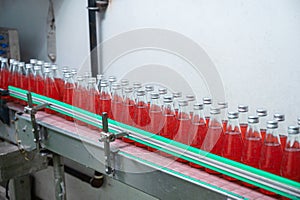 Glass bottled red juice on steel conveyor of production line in beverage processing factory