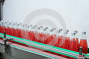 Glass bottled red juice on steel conveyor of production line in beverage processing factory