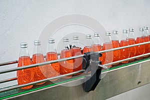 Glass bottled red juice on steel conveyor of production line in beverage processing factory