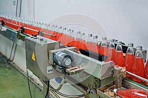 Glass bottled red juice on steel conveyor of production line in beverage processing factory