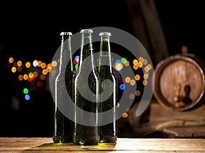 Glass bottles of beer and wooden barrel on bar lights background