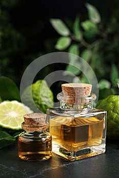 Glass bottles of bergamot essential oil and fresh fruits on black stone table