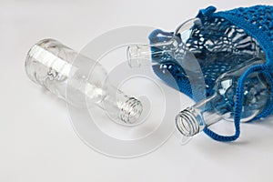 Glass bottles in a blue string bag on a white background, close-up - the concept of separate garbage collection