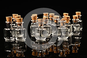 Glass bottles with cork on a black mirror surface with reflections isolated on black background