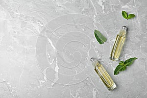 Glass bottles of essential oil, mint leaves on grey background, flat lay