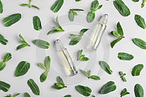 Glass bottles with essential oil among mint leaves on light background