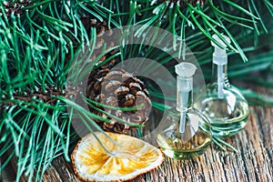 Glass bottles of essential oil with pine cones, oranges and fir branches on wooden background