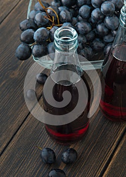 Glass bottles of fresh young red wine with a bunch of black grapes