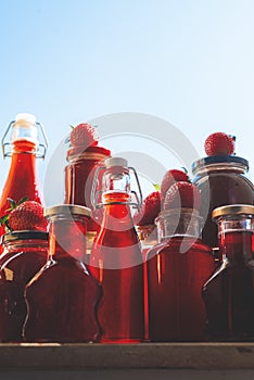 Glass bottles and jars with strawberries syrup and jam