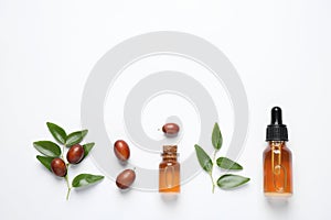 Glass bottles with jojoba oil and seeds on background, top view