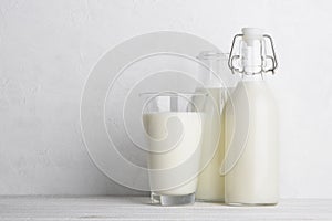 Glass and bottles of milk on white wooden table background
