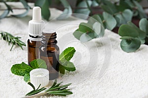 glass bottles with natural essential oils on a white towel with mint, rosemary and eucalyptus leaves