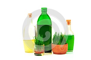 Glass bottles with oil and juice and sprouts of wheat in wooden bowl isolated on white background