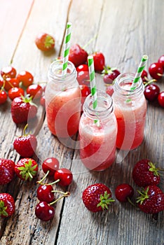 Glass bottles with a red smoothies made with red berries and fruits.