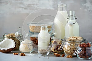 Glass bottles of vegan plant milk and almonds, nuts, coconut, hemp seed milk on grey concrete background. Banner with copy space.