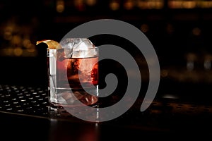 Glass of a Boulevardier cocktail with orange zest on the steel bar counter