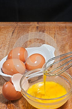 Glass bowel of egg with chef`s hand and whisk, egg shell and three brown eggs