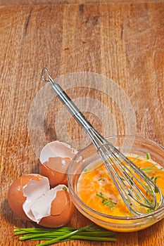 Glass bowel of egg with whisk, egg shell on wood cutting board