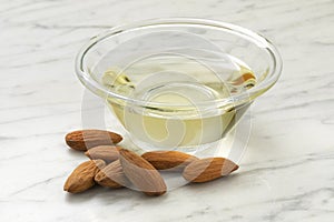 Glass bowl with almond oil and a heap of almonds close up