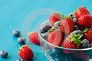 Glass bowl with assortment berries blueberries, strawberries over wooden table. Natural day light. Top view