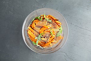 Glass bowl with baked sweet potato slices and arugula on grey background