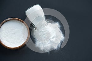 Glass bowl of baking soda. Spoonful of bicarbonate. Top view, flat lay. Close up on a black background. copy space for
