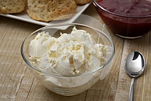 Glass bowl with clotted cream in front of scones close up photo