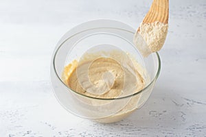 Glass bowl with dough and spatula, dough texture and consistency, light blue background. The stage of preparing homemade