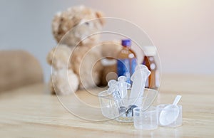 glass bowl filled with many syringe on the burred background of a teddy bear with child medicine bottles