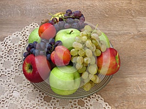 A glass bowl of fresh organic autumn fruit on crochet table cloth and oak wood table background.