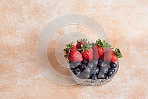 Glass bowl with fresh strawberries and blueberries on an abstract background of pastel colors and copy space
