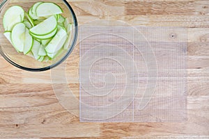 Glass bowl full of granny smith apple slices on a butcher block table, and slices laid out on a mesh tray ready for dehydrating ap