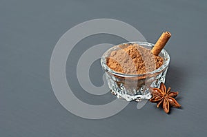 Glass bowl full of powder with cinnamon stick near star of anise lies on dark scratched desk on kitchen