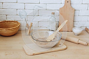 Glass bowl with groats and various kitchen utensils and dishware on wooden table