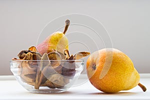 Glass bowl with homemade dried organic pear slices with fresh pears on white background