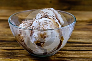 Glass bowl with ice cream balls and chocolate topping on a wooden table