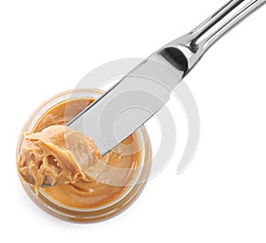 Glass bowl and knife with tasty peanut butter on white background, top view