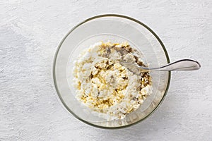 Glass bowl with mixed cottage cheese, eggs and vanilla sugar on a light gray background, top view. Cooking stage